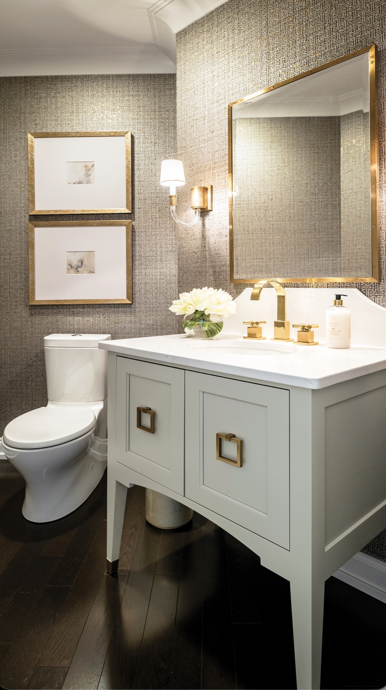 Tailored bathroom vanity with brass fixtures, framed mirror and patterned wallcovering